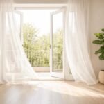 A wide open window in a clean minimal living space, sheer white curtains gently moving in a spring breeze. Gleaming floors below, a potted fiddle leaf fig in the corner, soft diffused daylight filling the room. Cream and warm white tones