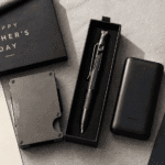 Neatly arranged Father's Day gift flatlay on a light grey linen surface, featuring a slim metal wallet, a multitool pen in a gift box, a compact power bank, and small cologne sample vials, warm natural window light, styled like a lifestyle magazine, top-down angle.