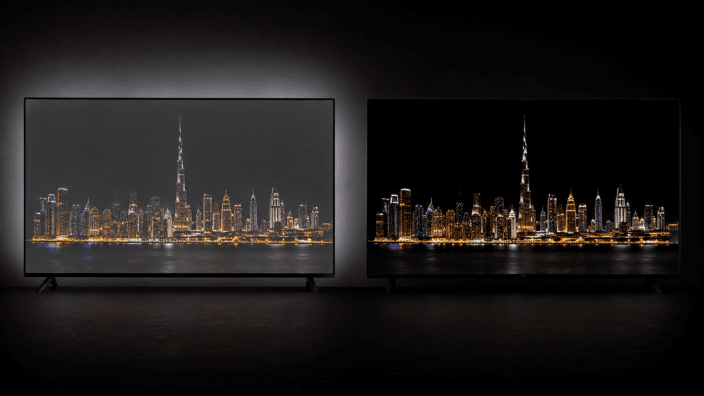 side-by-side comparison of two TVs on a dark studio backdrop. Left screen shows a night cityscape with grey washed-out blacks and visible backlight glow. Right screen shows the identical scene with perfect black sky and vivid punchy city lights floating in total darkness