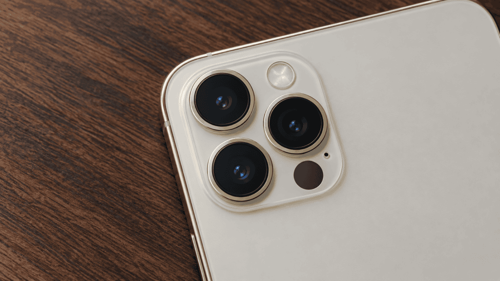 Back of an iPhone Pro on a wooden table, with three camera lenses and the small dark LiDAR scanner beside them.
