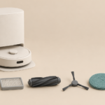 A white robot vacuum on its self-empty dock, with a dust bag, filter, main brush, side brush, mop pad and bottle laid out in a row.